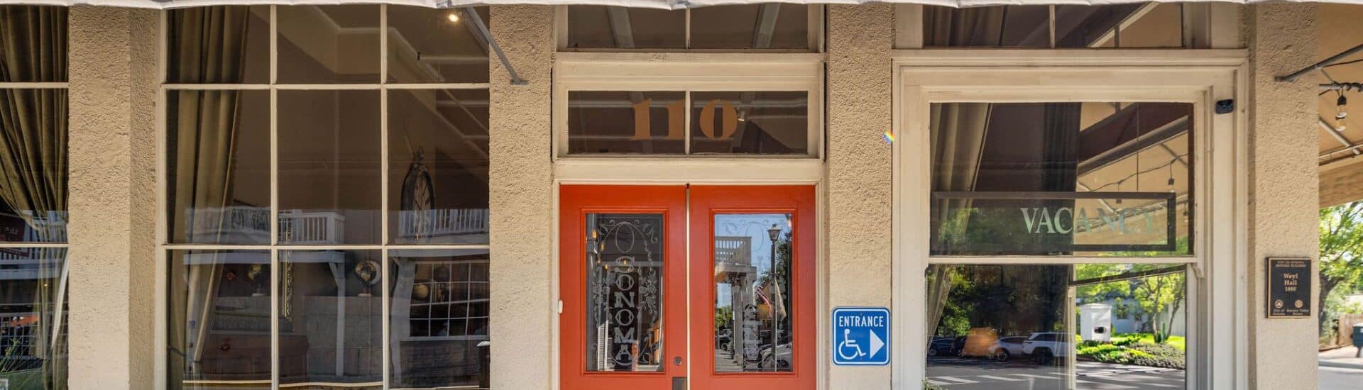Front facade of a hotel with large paned windows, orange door and canopy with hotel name