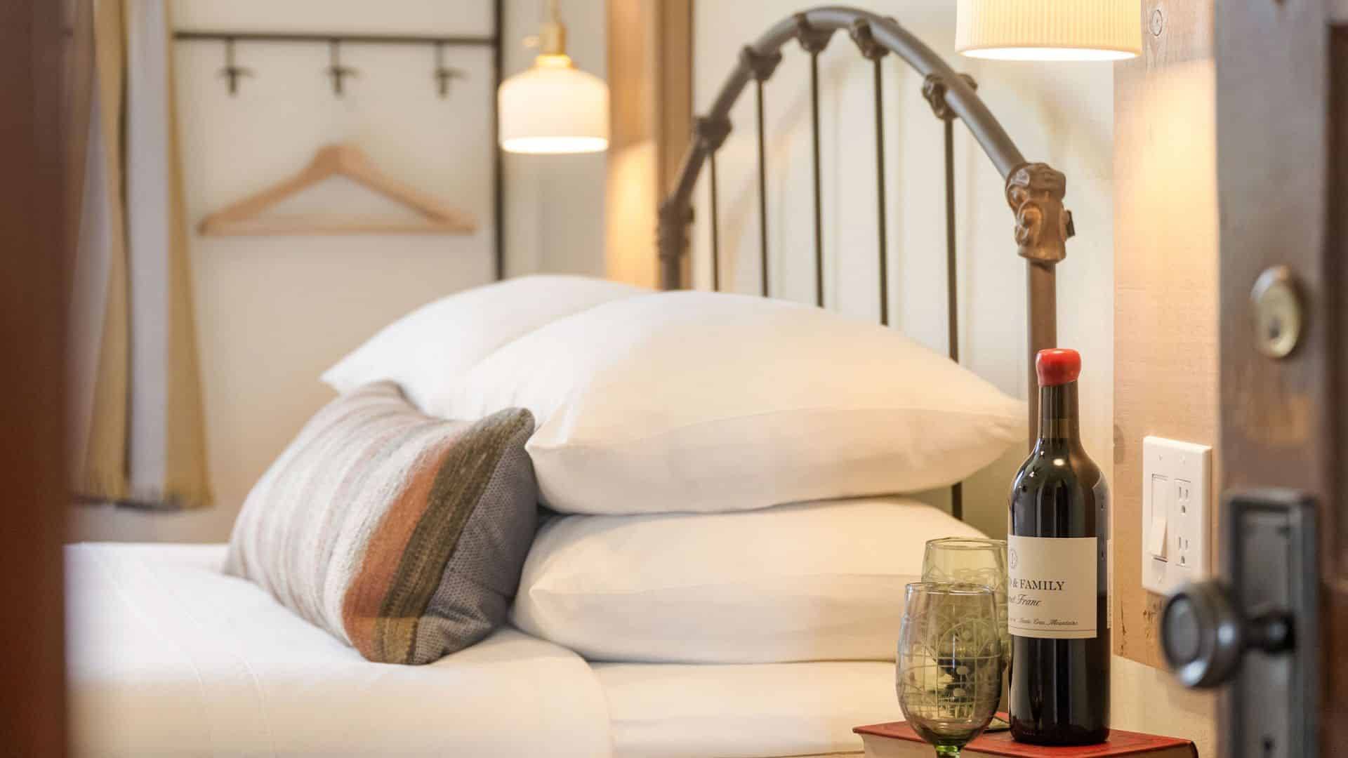 Bed with a curved headboard, white pillows and linens. side table with bottle of wine and two glasses